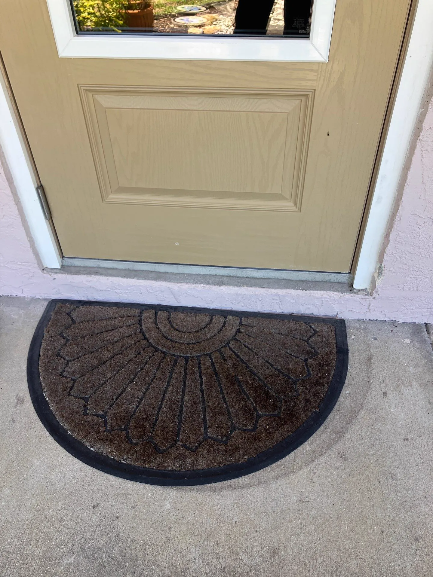 The lower half of a tan front door with a recessed rectangular panel, set in white trim with a metal threshold at the bottom, above a half-round doormat on a concrete entry.